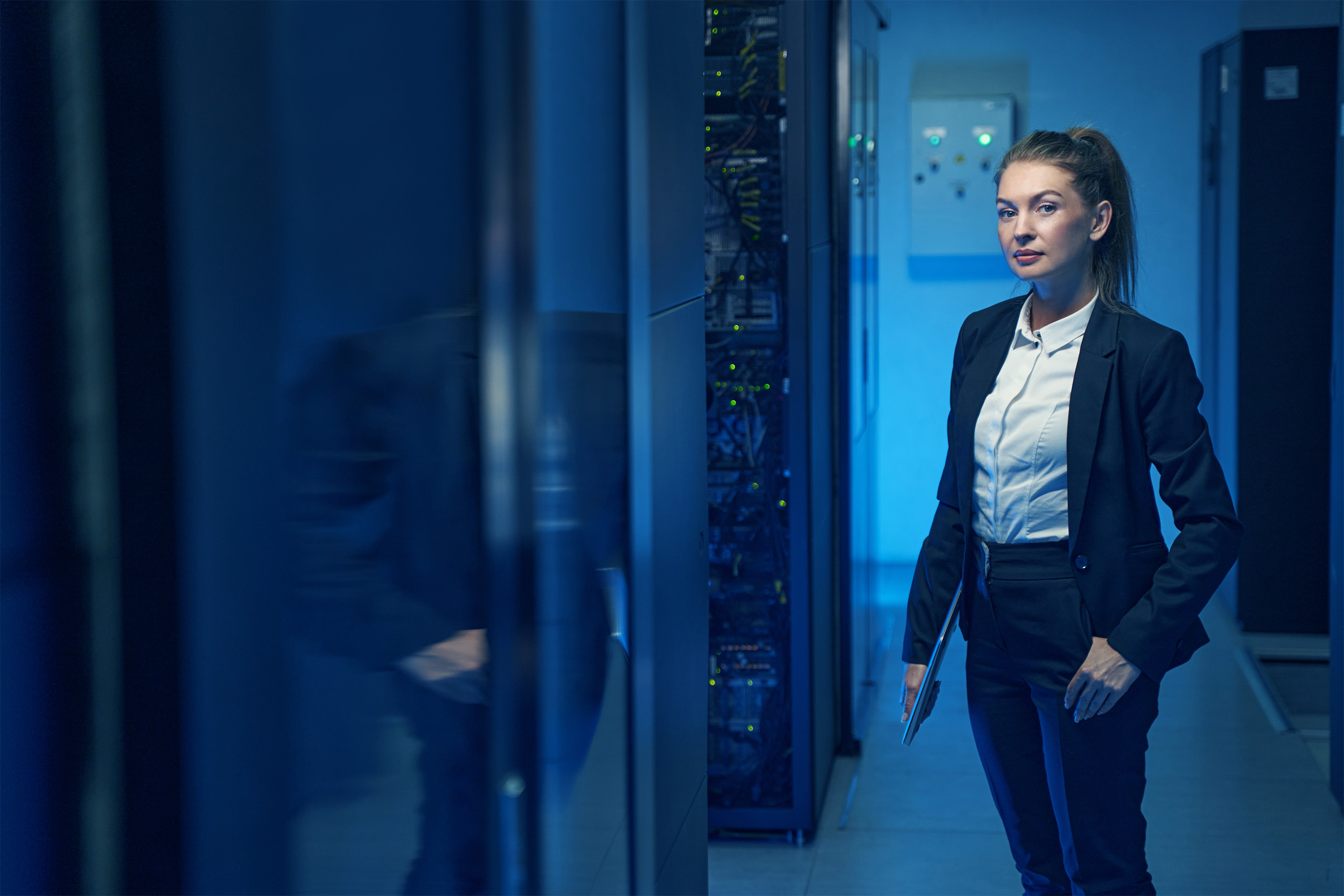Confident woman engineer standing near server racks in datacenter